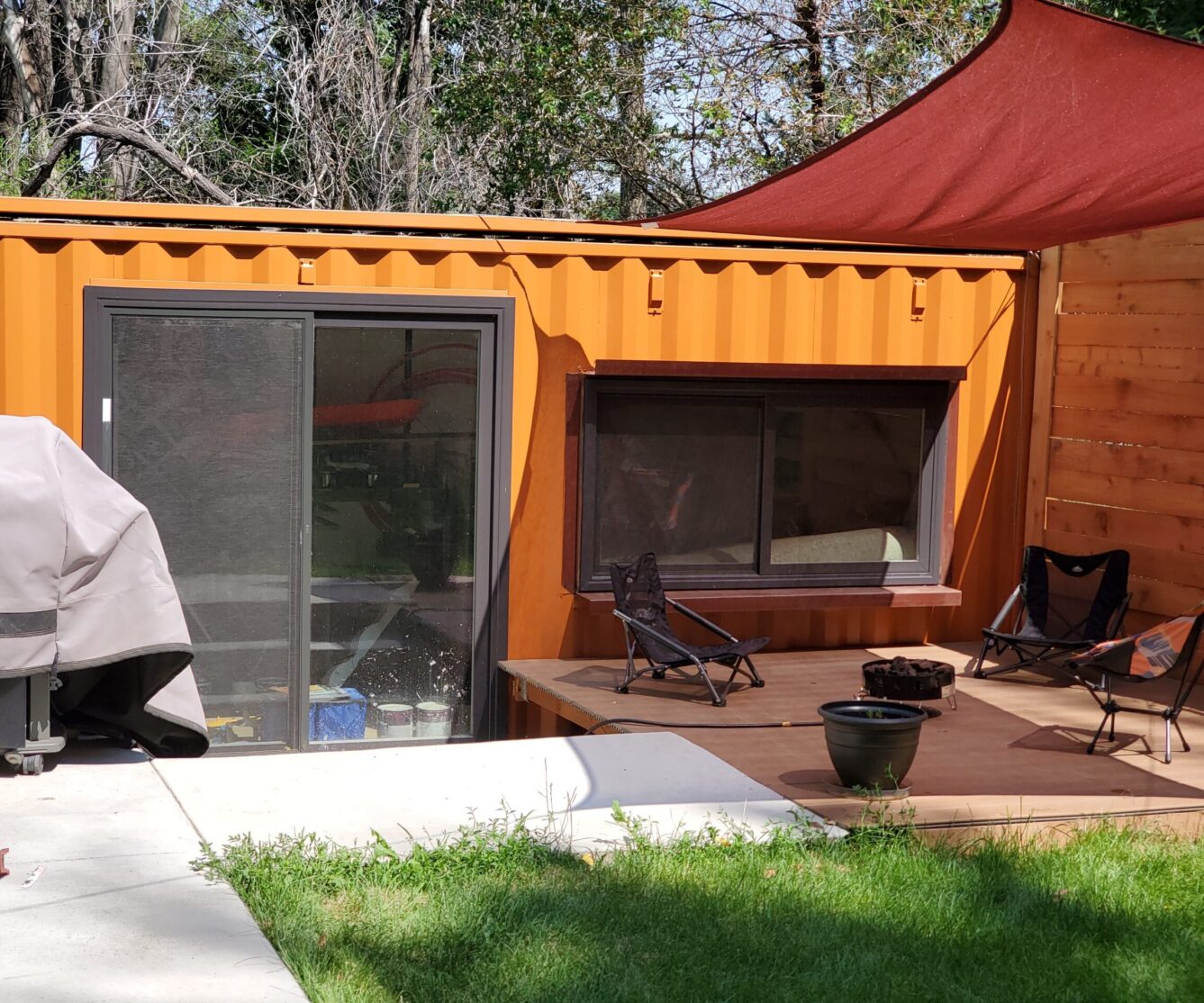A sunny patio built alongside an orange shipping-container dwelling.